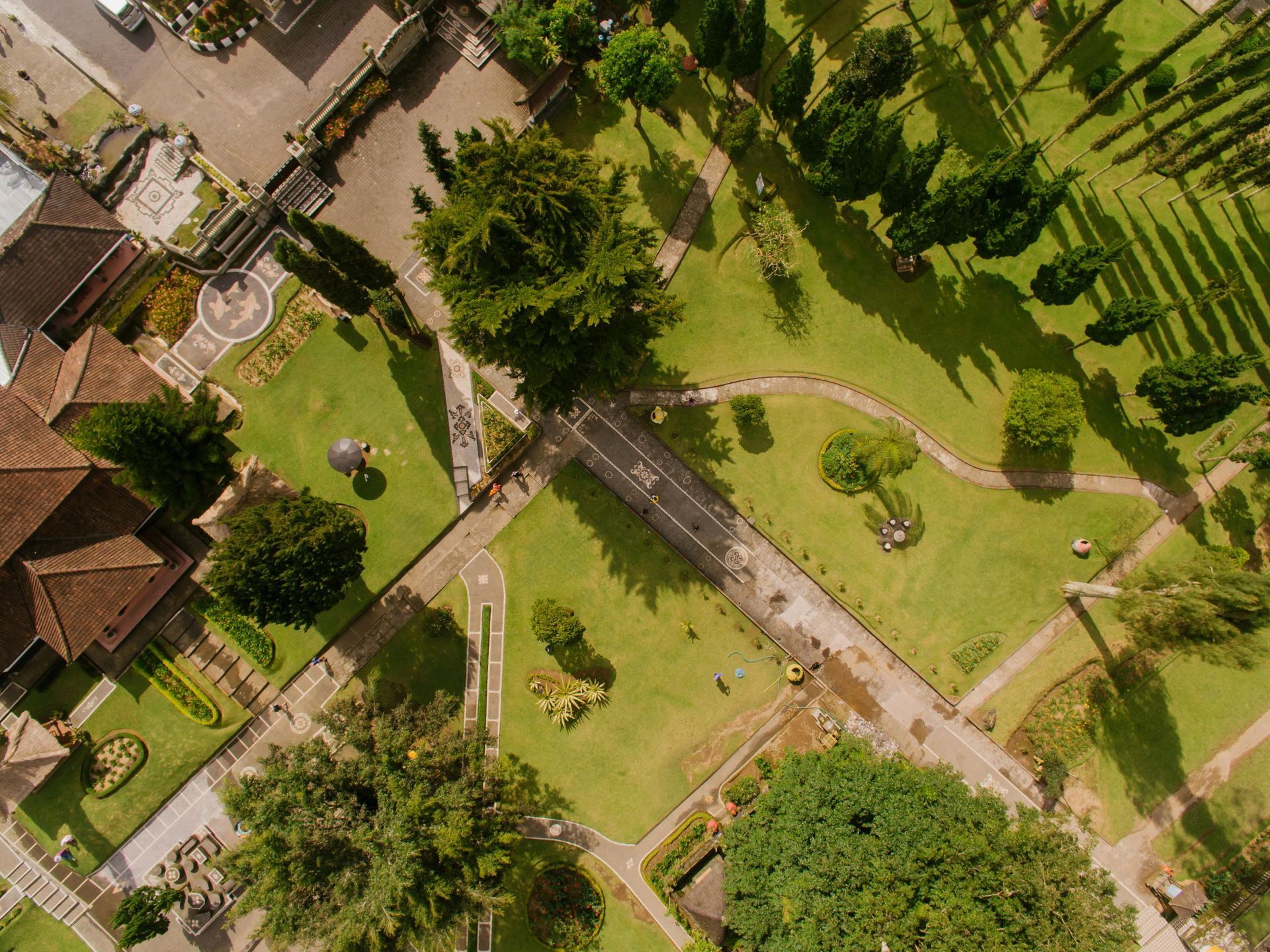 Aerial view of a park with green lawns, trees, and walkways; several buildings with red roofs.