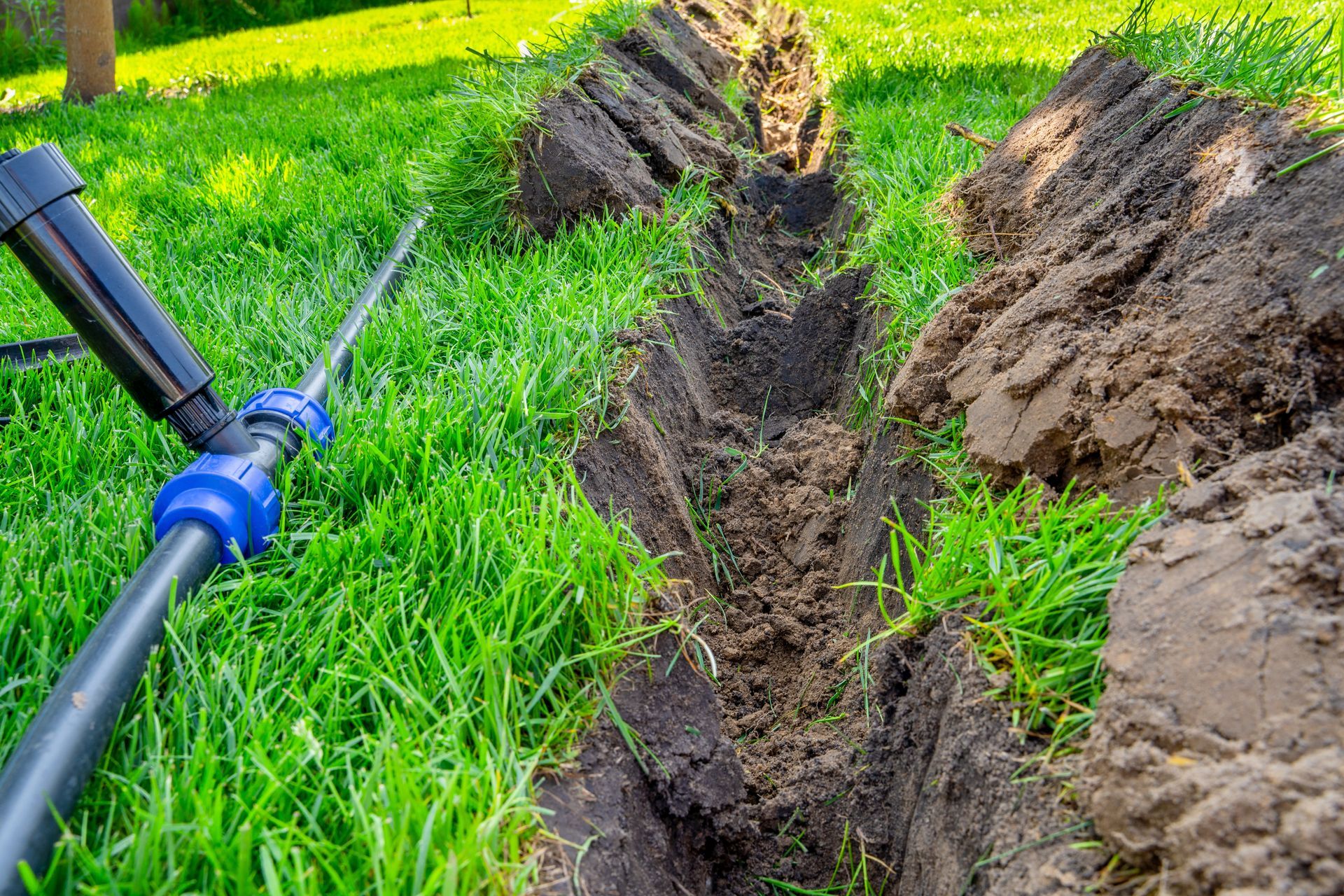 A blue irrigation pipe beside a freshly dug trench in a green field