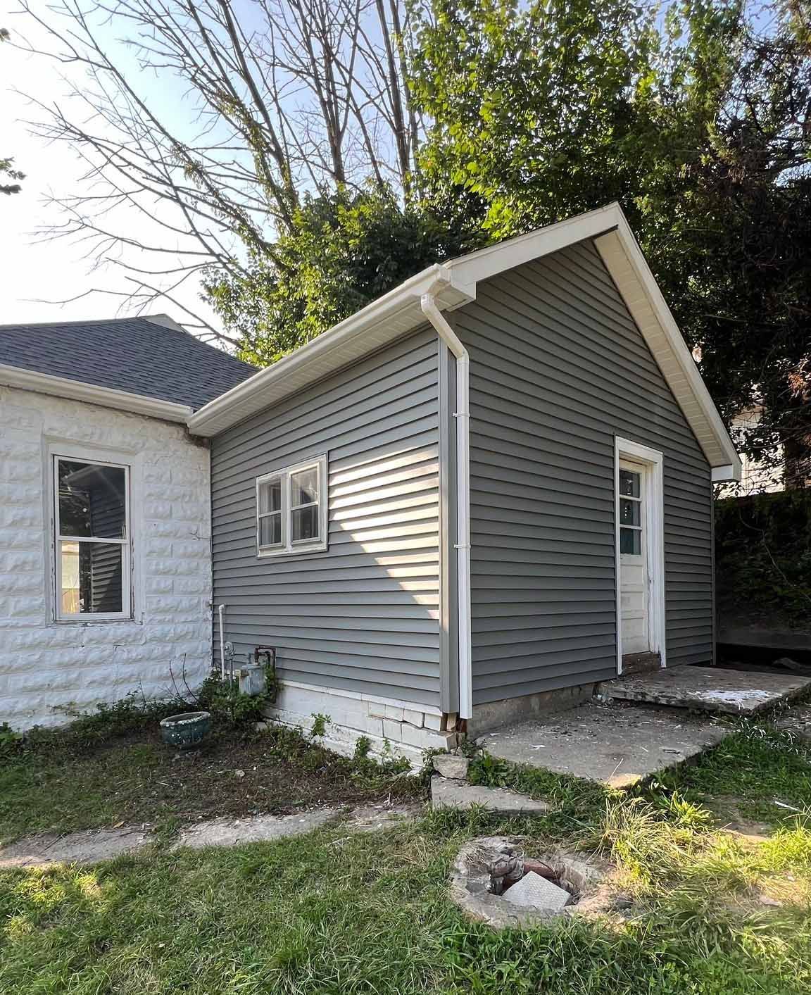 A small house with a gray siding and a white door