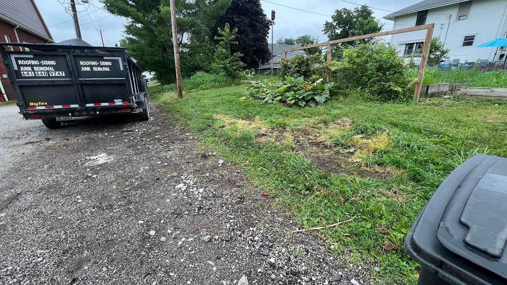 A dumpster is parked in the grass next to a trash can