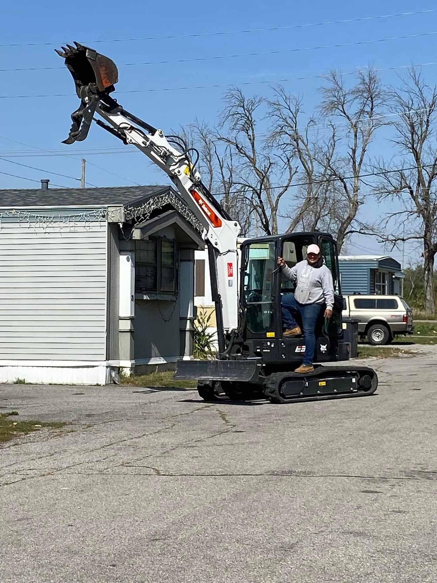 A man is driving a small excavator in front of a house