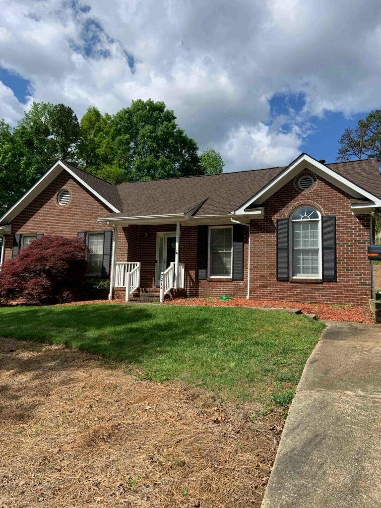 A brick house with a brown roof and black shutters is for sale.