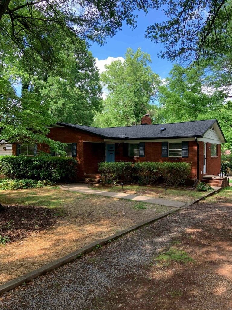 A brick house with a driveway leading to it is surrounded by trees.