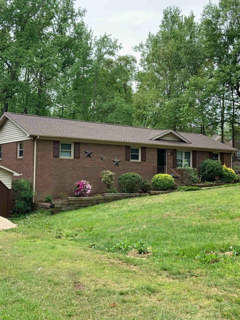 A brick house with a brown roof and a large lawn in front of it.