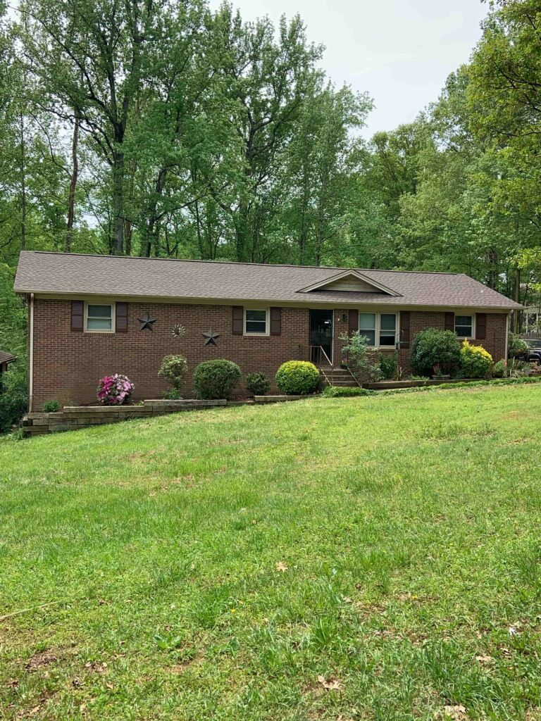A brick house with a roof and a large lawn in front of it.