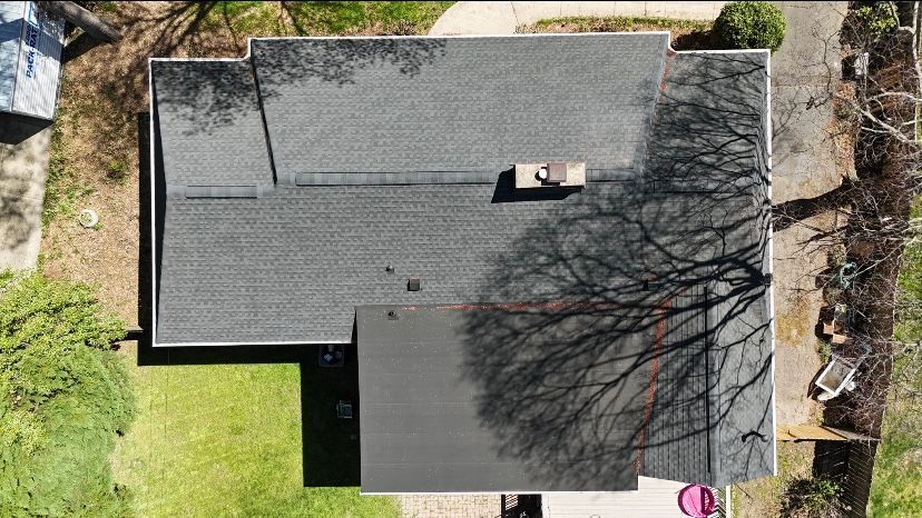 Overhead view of a house with gray shingle roof and a flat, dark roof extension. A large tree casts a shadow.