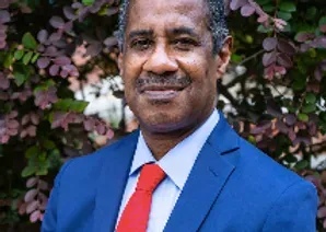 A man in a blue suit and red tie is standing in front of a tree.