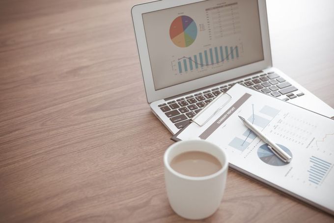 A Laptop With a Pie Chart on the Screen Next to a Cup of Coffee — D&T Accounting & Bookkeeping In Umina Beach, NSW