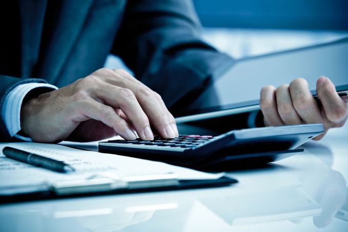 A Man in a Suit is Using a Calculator at a Desk — D&T Accounting & Bookkeeping In Umina Beach, NSW