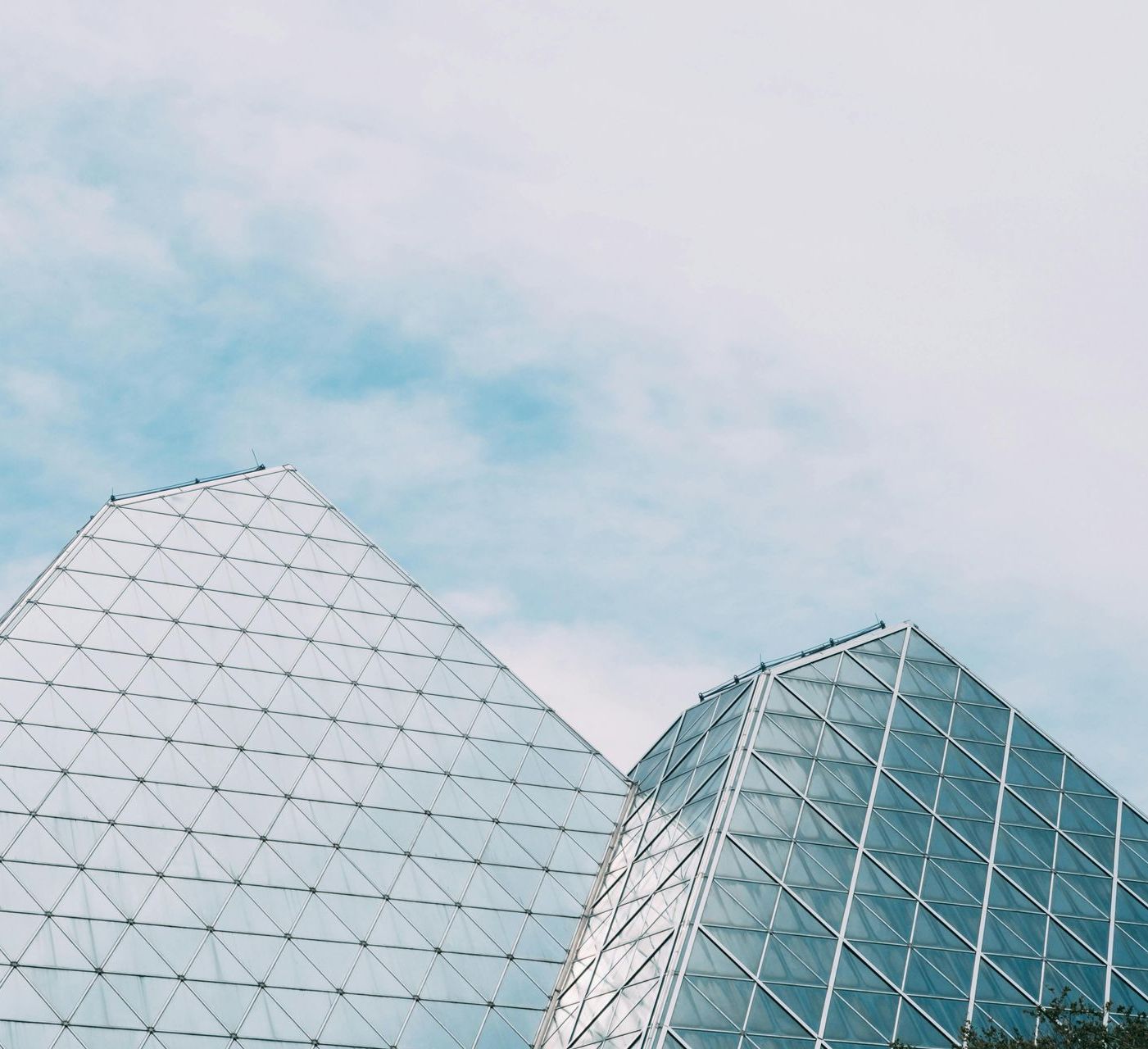 Two glass pyramids against a blue sky with clouds