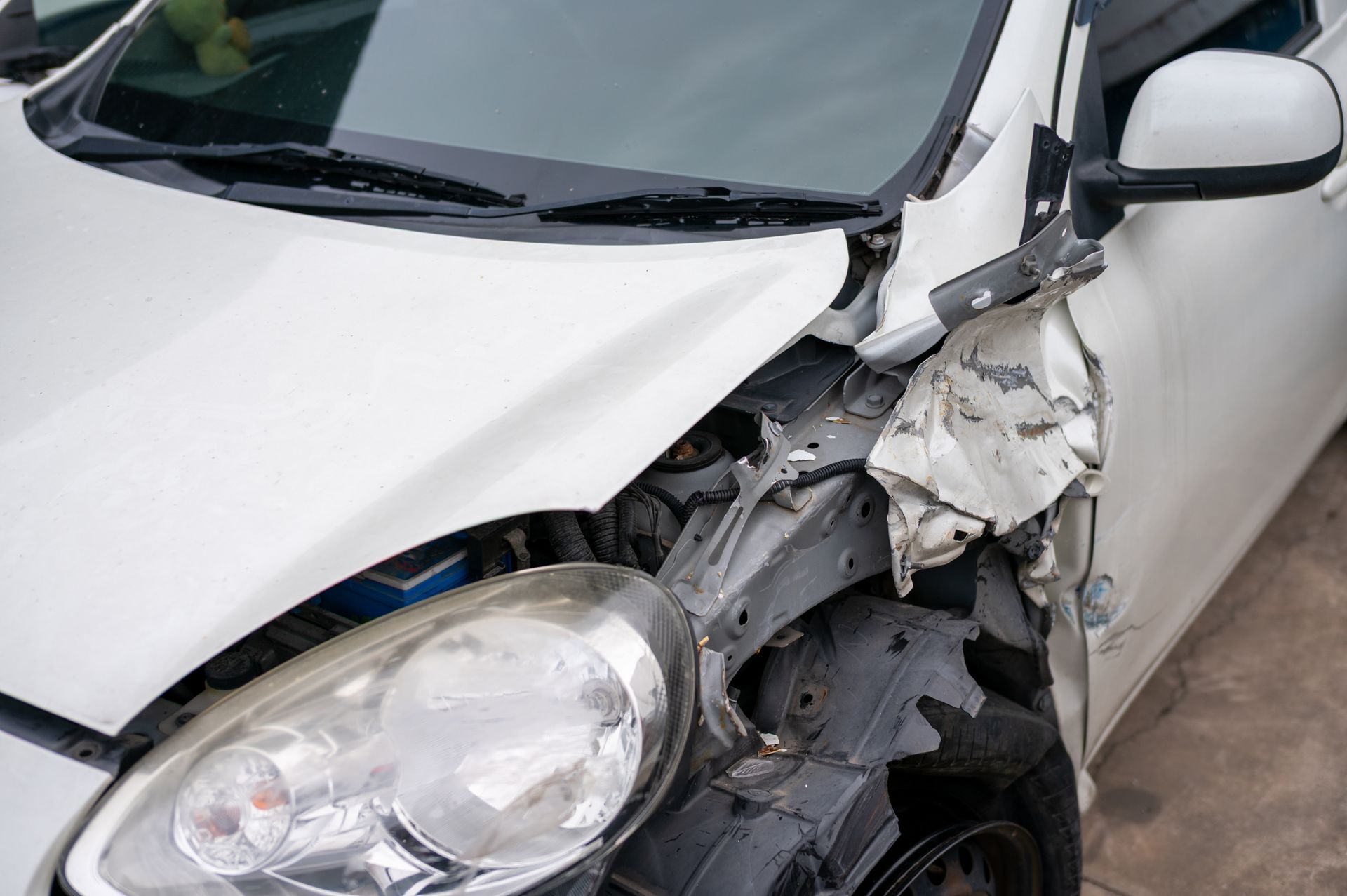 White car damaged on the front right side after a collision; the headlight is visible.