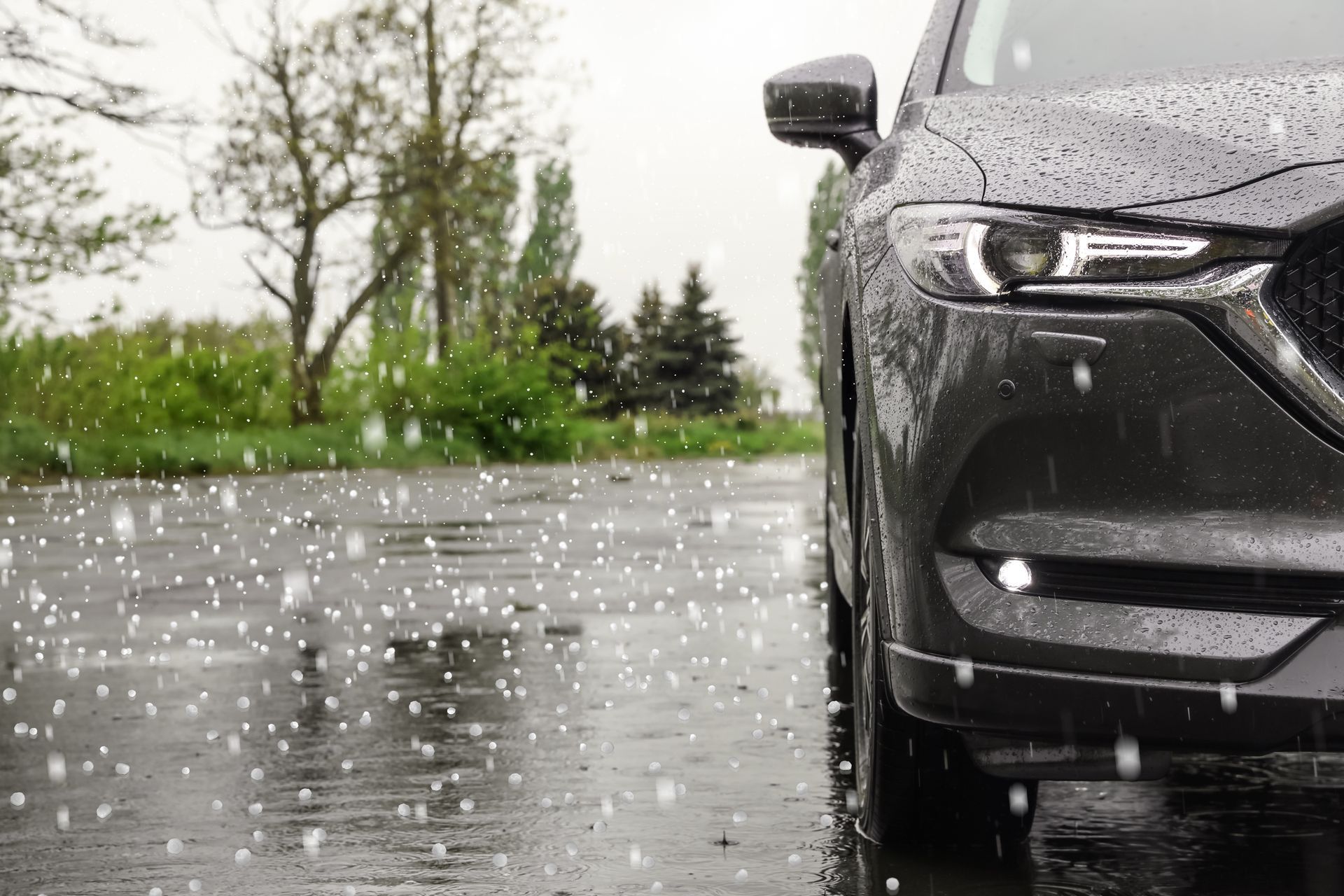 Gray SUV parked on a wet road, with hail falling. Trees and greenery are in the background.