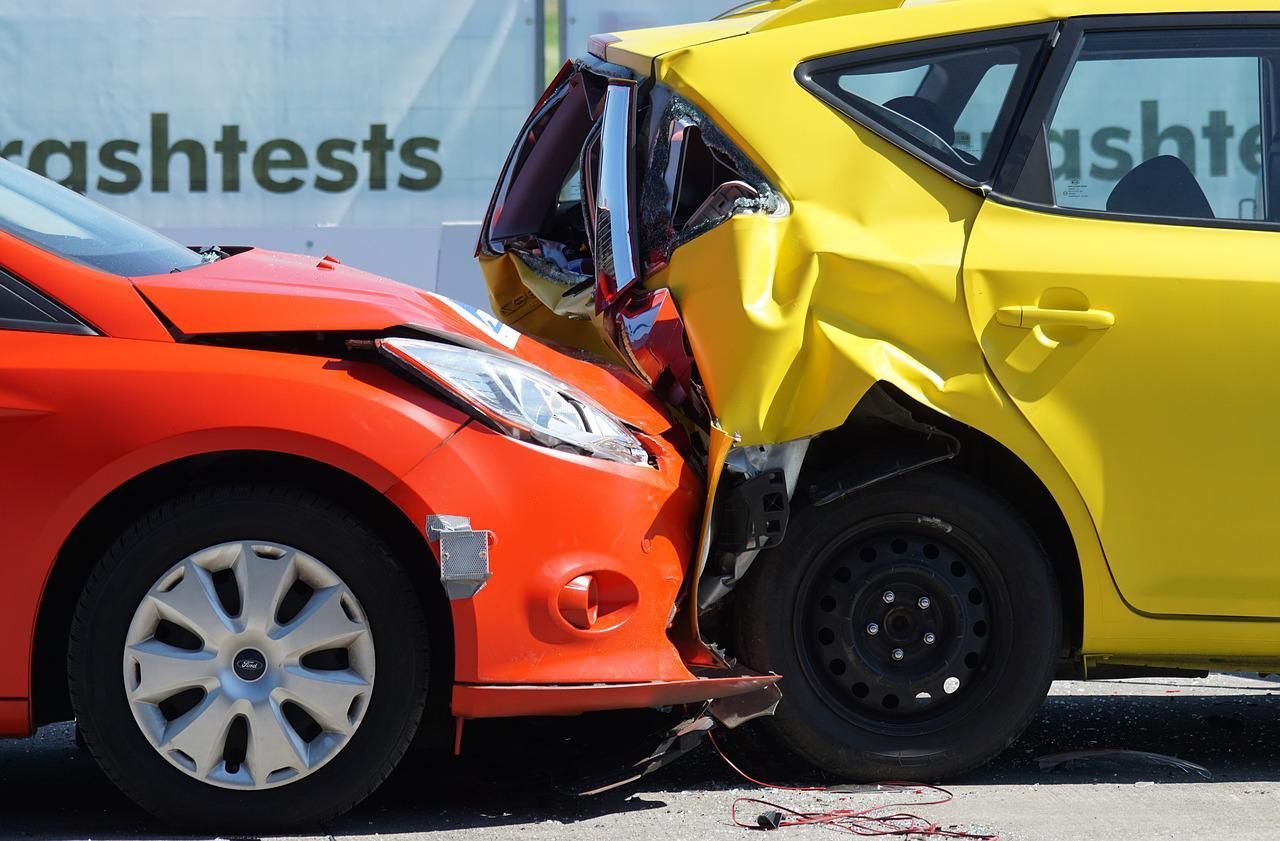 Orange car crashed into yellow car, damage visible, likely a crash test.