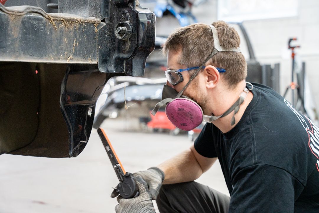 Mechanic wearing safety gear working on a car in a repair shop.