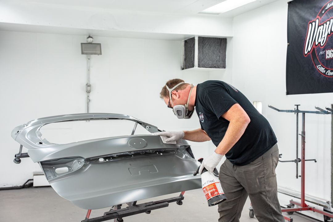 Person in respirator and gloves painting a car trunk in a workshop.