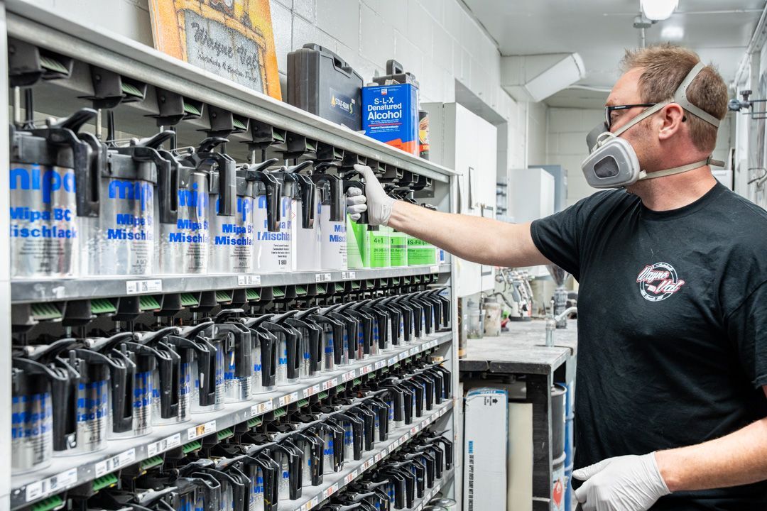 Man in respirator mask selects paint from shelf of spray cans in a workshop.