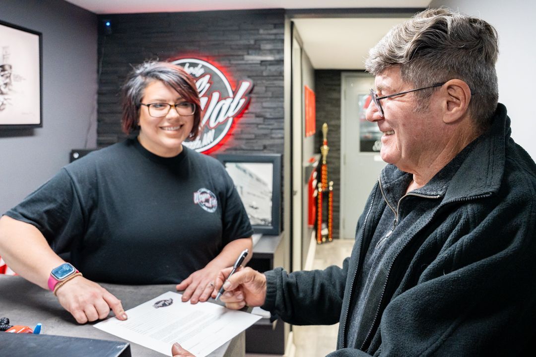 Woman behind counter assisting a customer signing paperwork. Red neon sign in background.