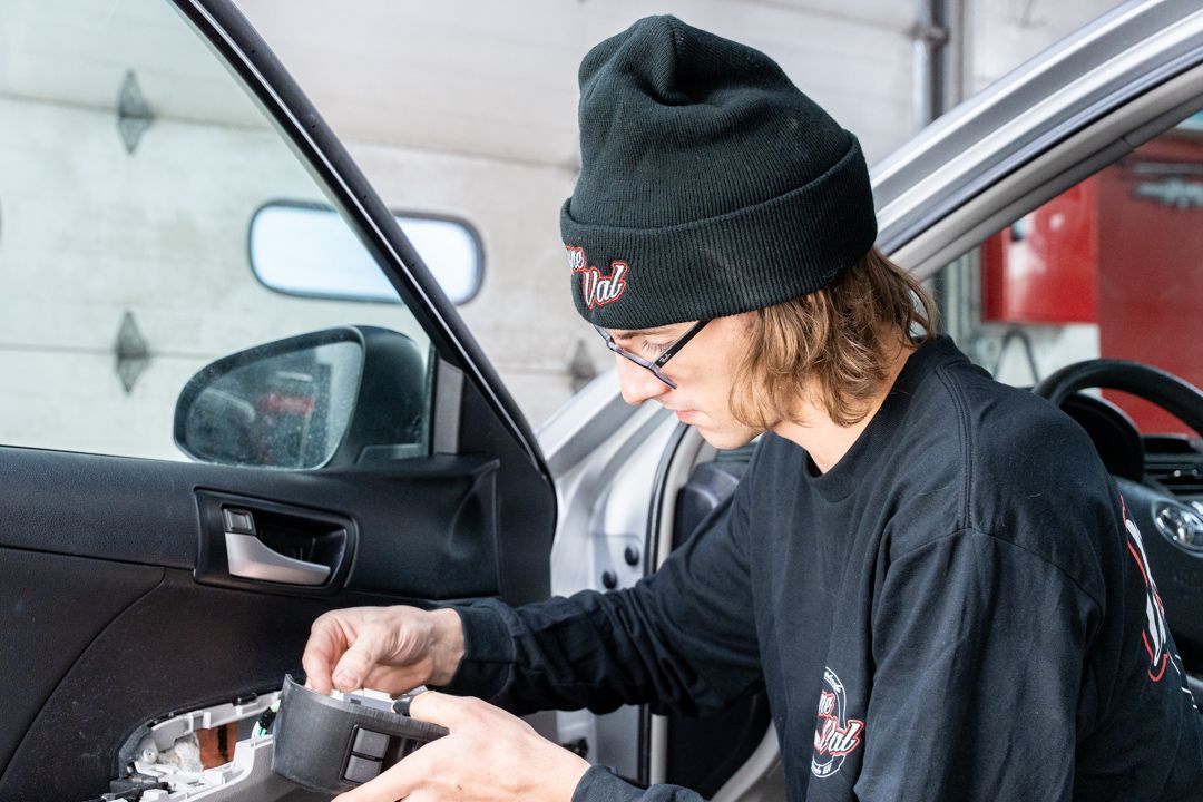 Mechanic in a black beanie and shirt, working on a car door in a garage.
