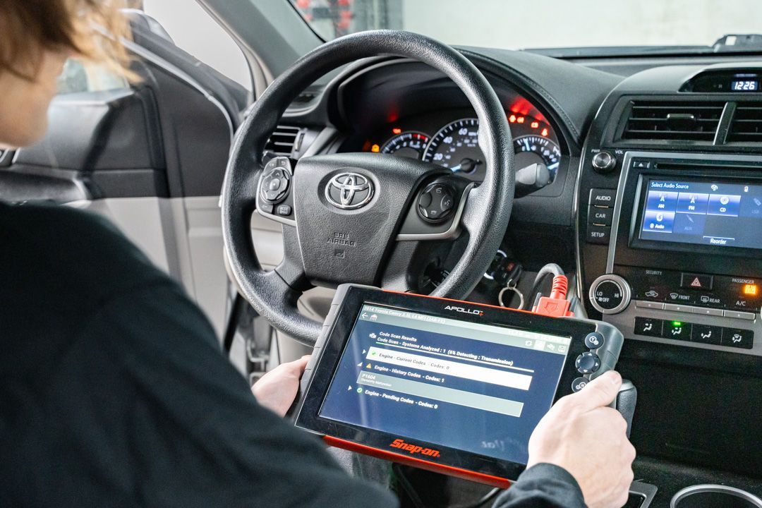 Person using a diagnostic tablet inside a Toyota car, checking dashboard lights.