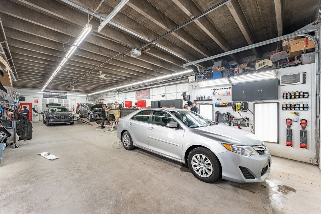 Inside a car repair shop, a silver sedan sits near the center. Other cars are visible along with tools and equipment.