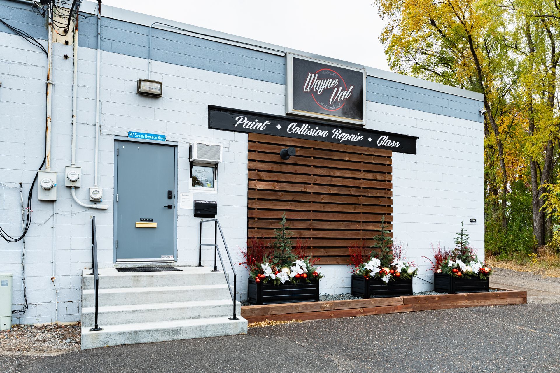 Exterior of a business with a sign: "Norman's Body Shop". White and gray building with a wooden accent and door.
