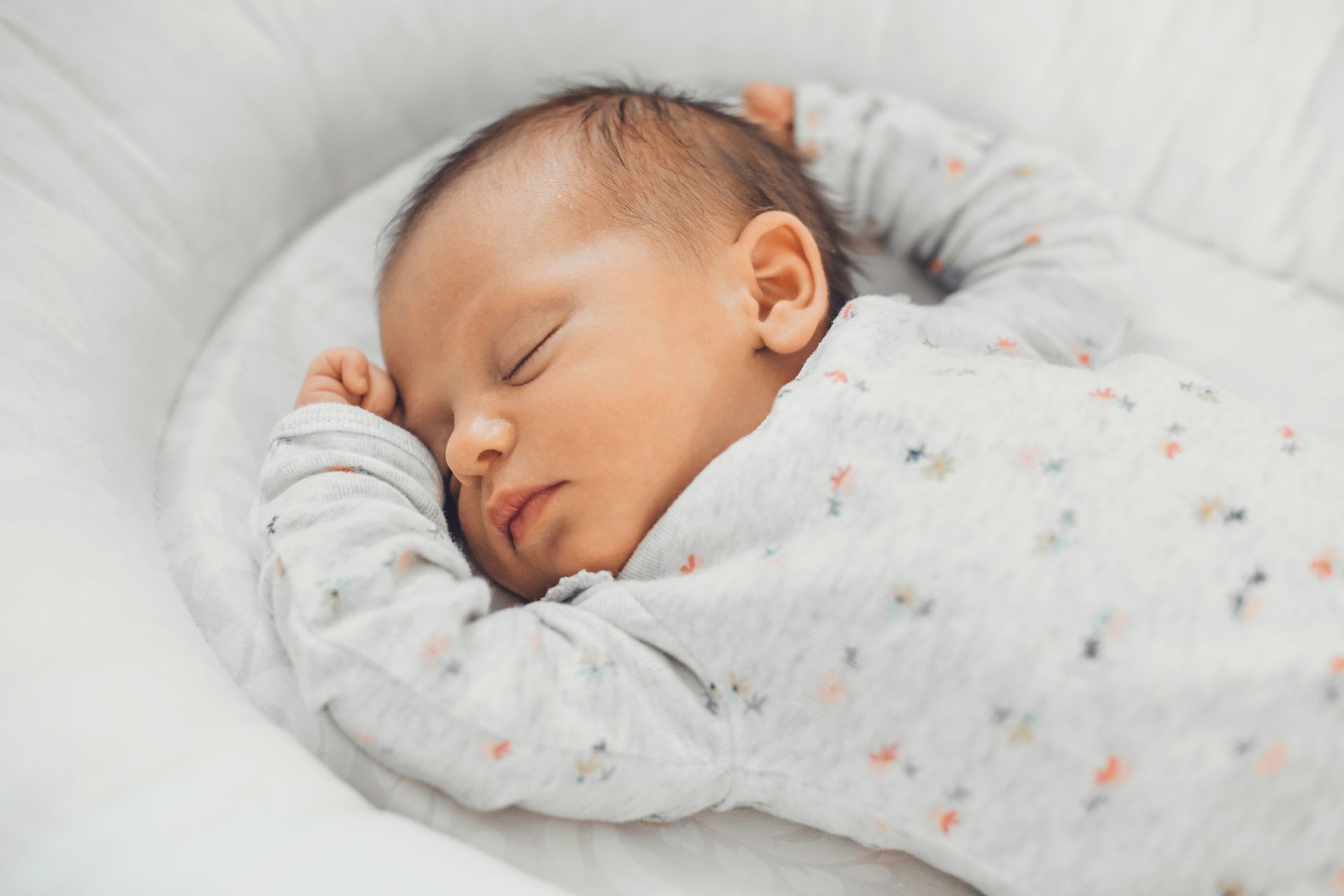 Smiling baby lying on white pillows and blanket in a bright bed