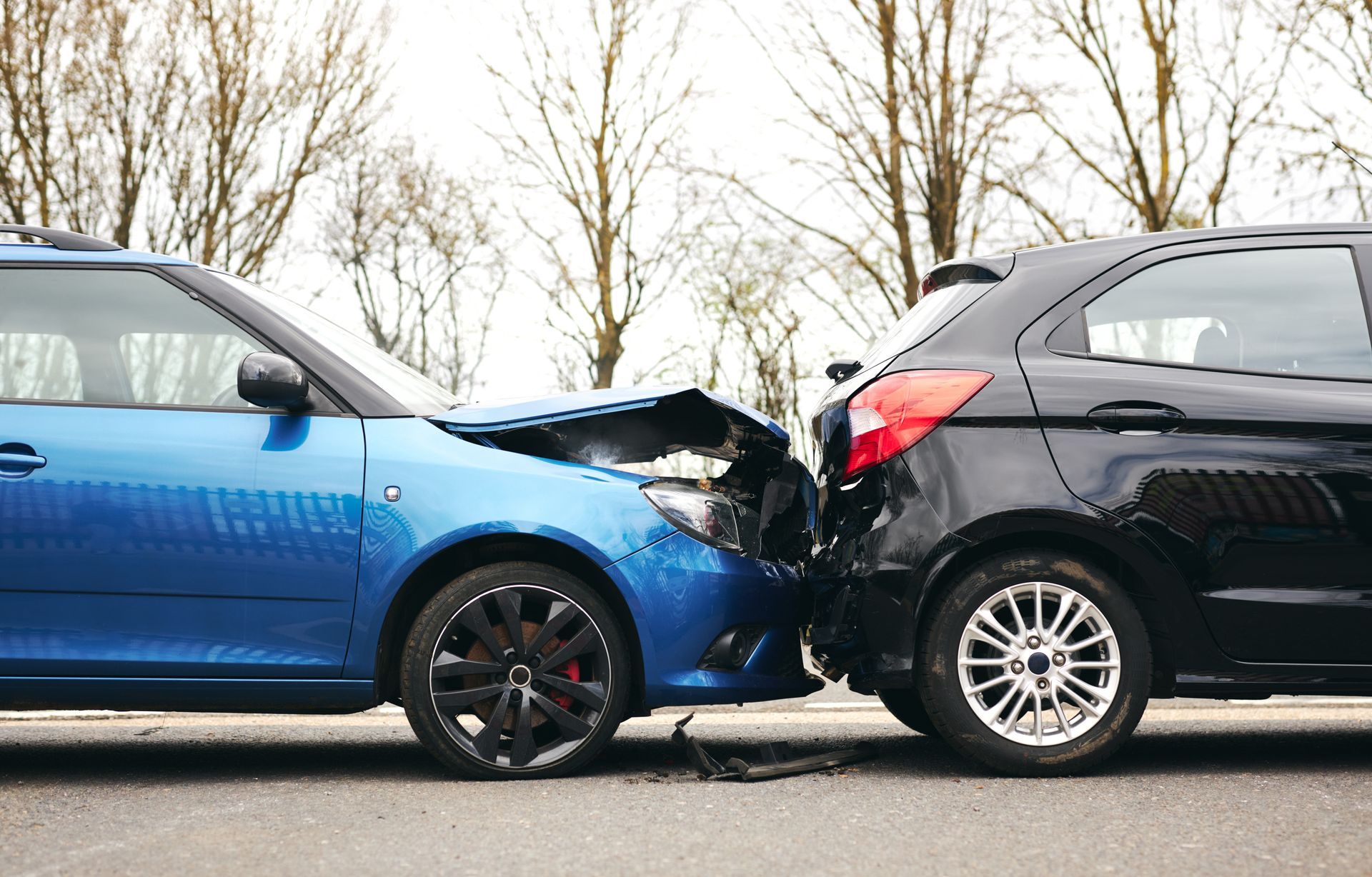 Two cars, blue and black, collided front-to-front on a road, with crumpled front ends.