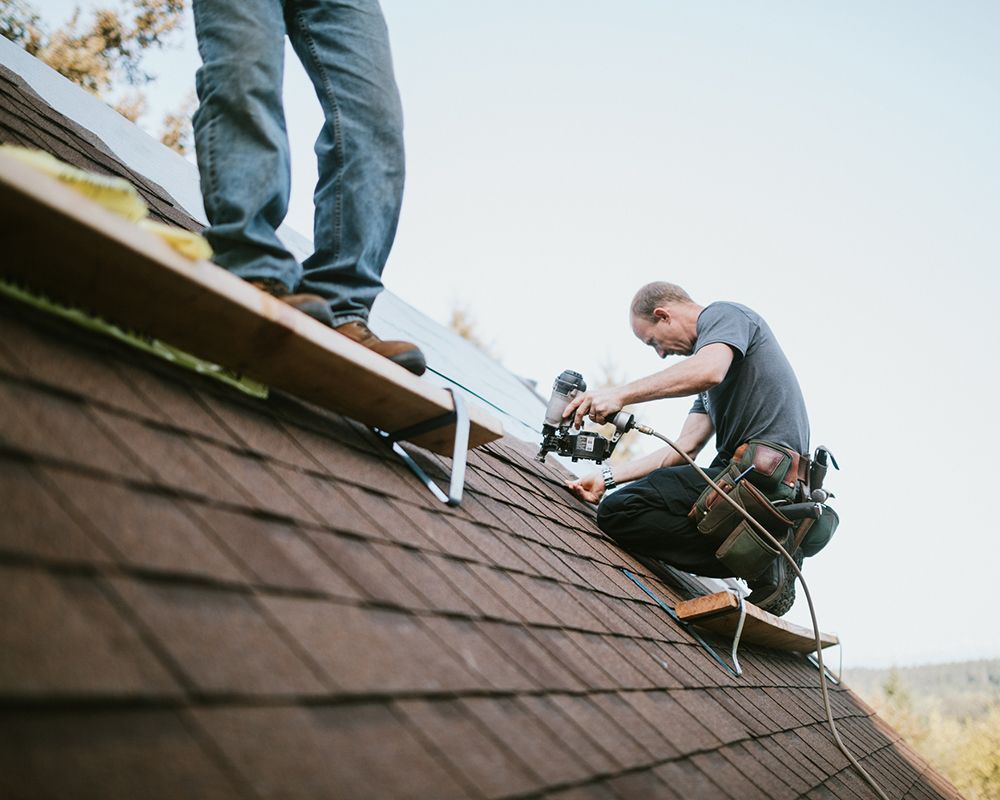 Two workers performing a commercial roof repair in Waverly, NE, using professional tools on a shingl