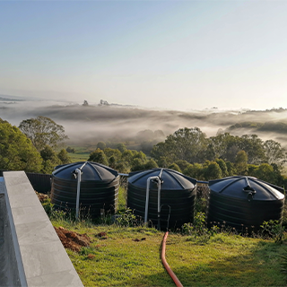 A Row Of Black Water Tanks Are Sitting On Top Of A Grassy Hill — Water Please In Ballina, NSW
