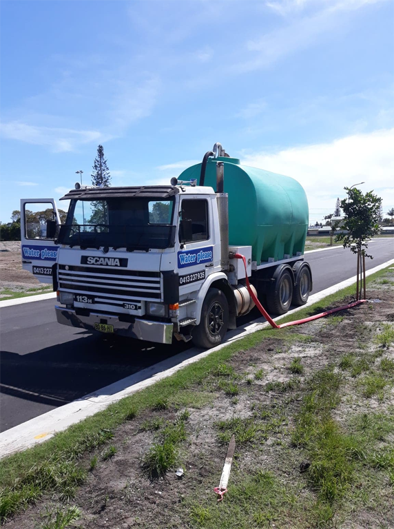 A Blue Tanker Truck is Driving Down a Street Next to a House — Water Please In Mullumbimby, NSW