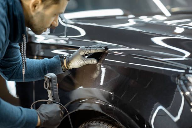 A man is polishing the fender of a black car.