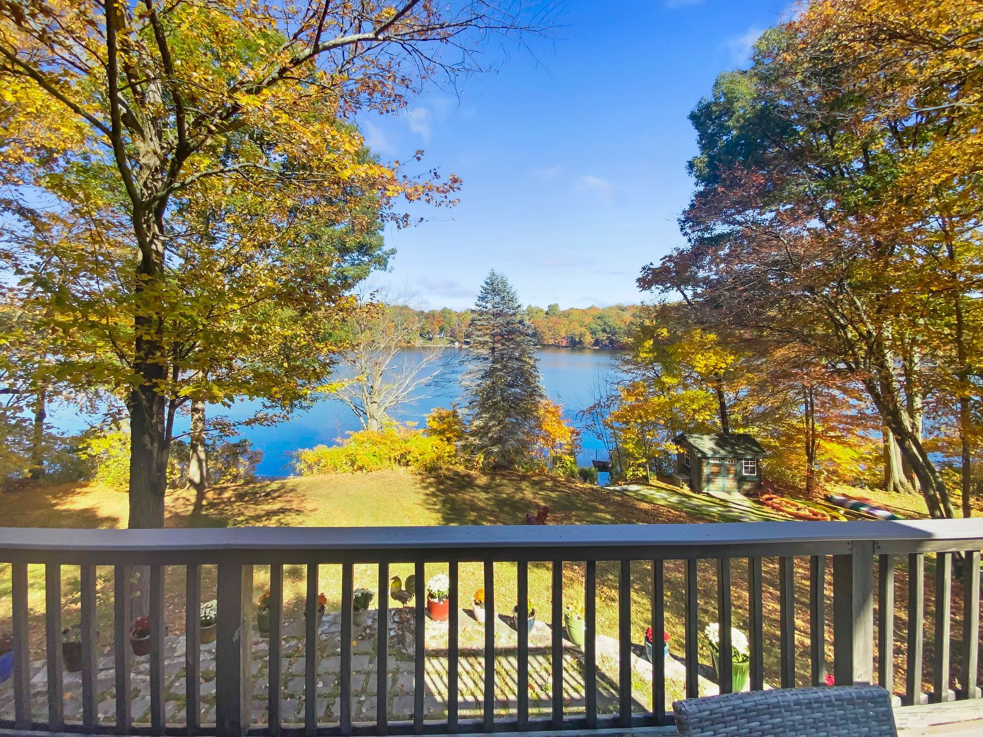 A scenic view of a blue lake framed by vibrant, autumnal trees, seen from a backyard wooden deck.