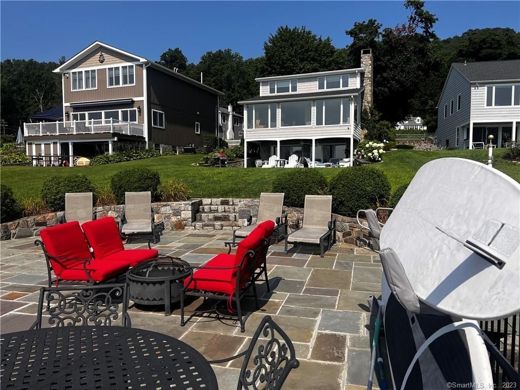 Patio with red cushioned chairs, outdoor furniture, and a sundial, with multi-story houses and trees in the background.