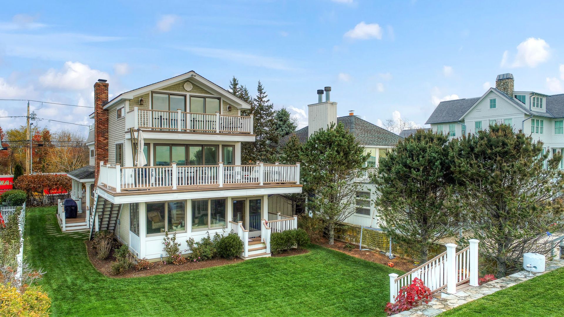 A three-story white house with balconies, large windows, and a chimney, set on a green lawn against a blue sky.
