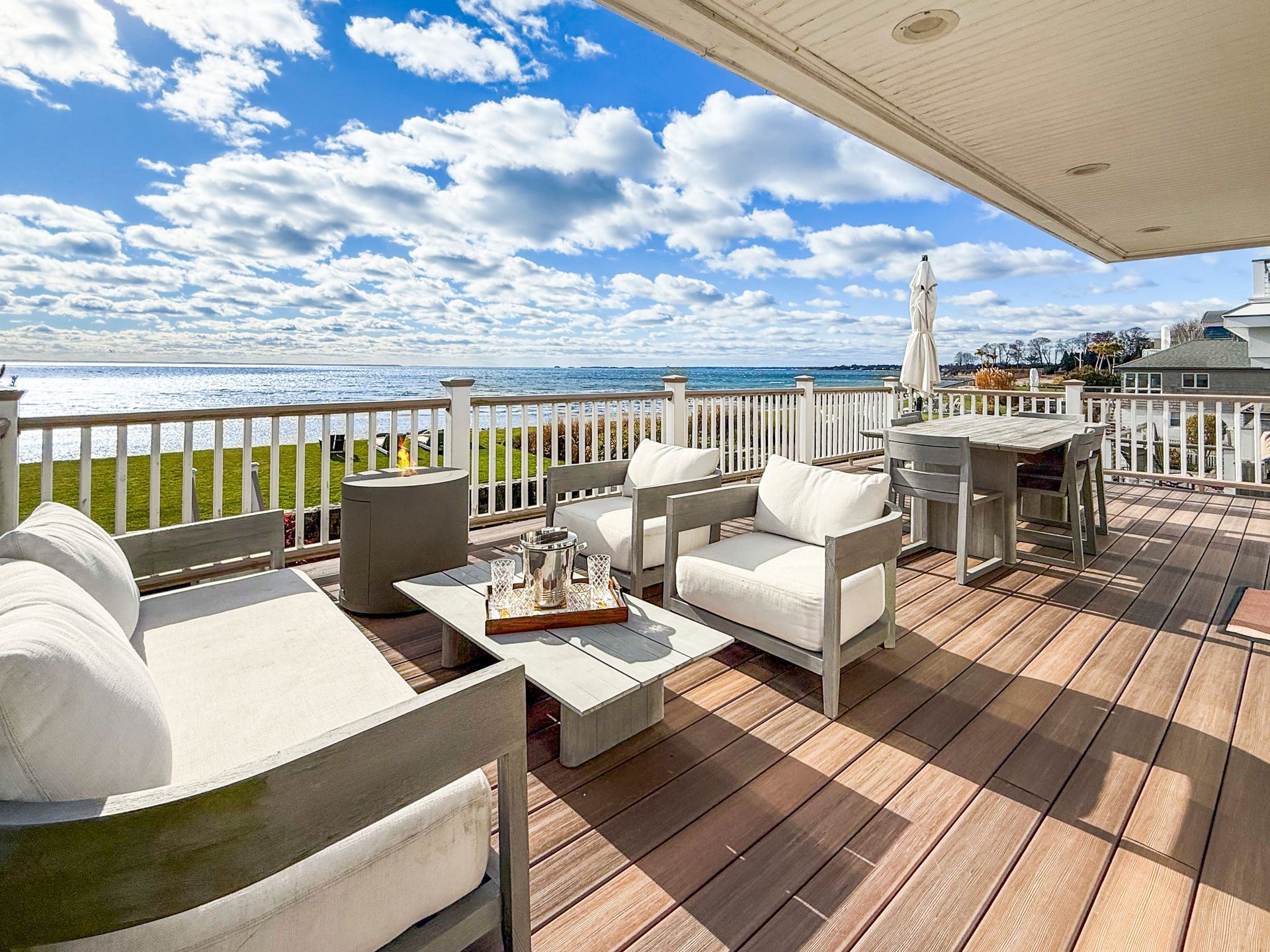 A spacious deck overlooking the ocean with patio furniture, including a white sofa, armchairs, and a dining table.