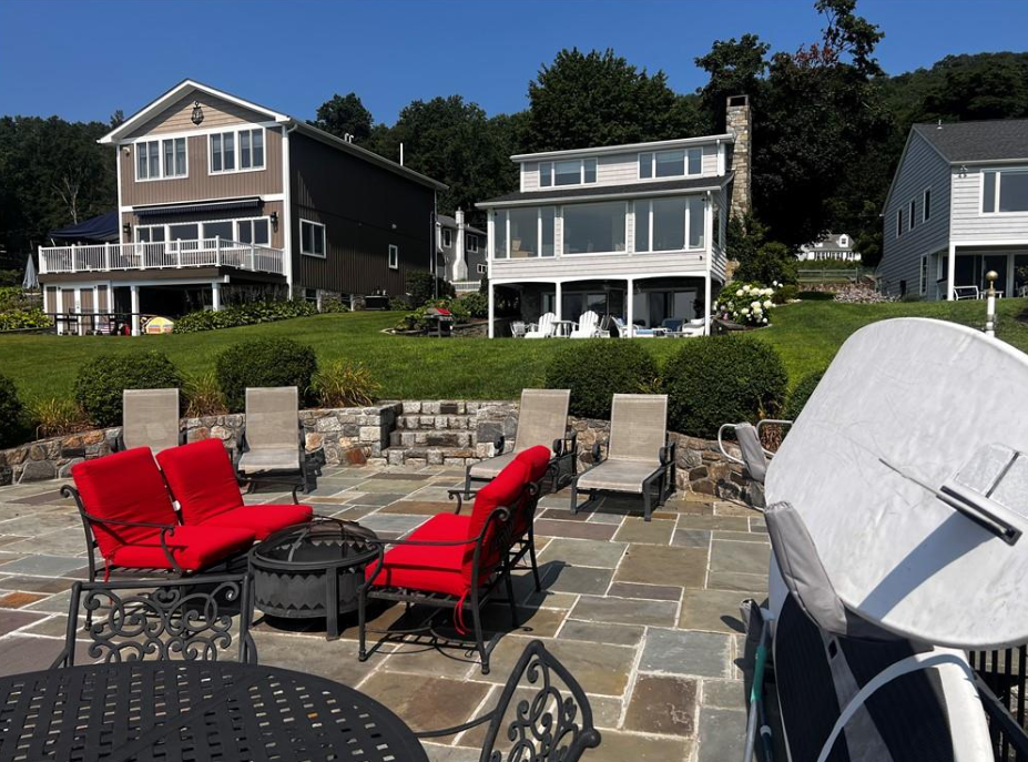 A stone patio features red outdoor furniture and lounge chairs, with houses in the background under a clear blue sky.