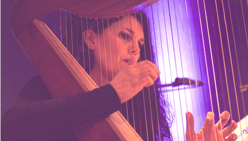 I am Charlotte playing a harp under purple lighting, with a focus on their hands and expression of concentration.