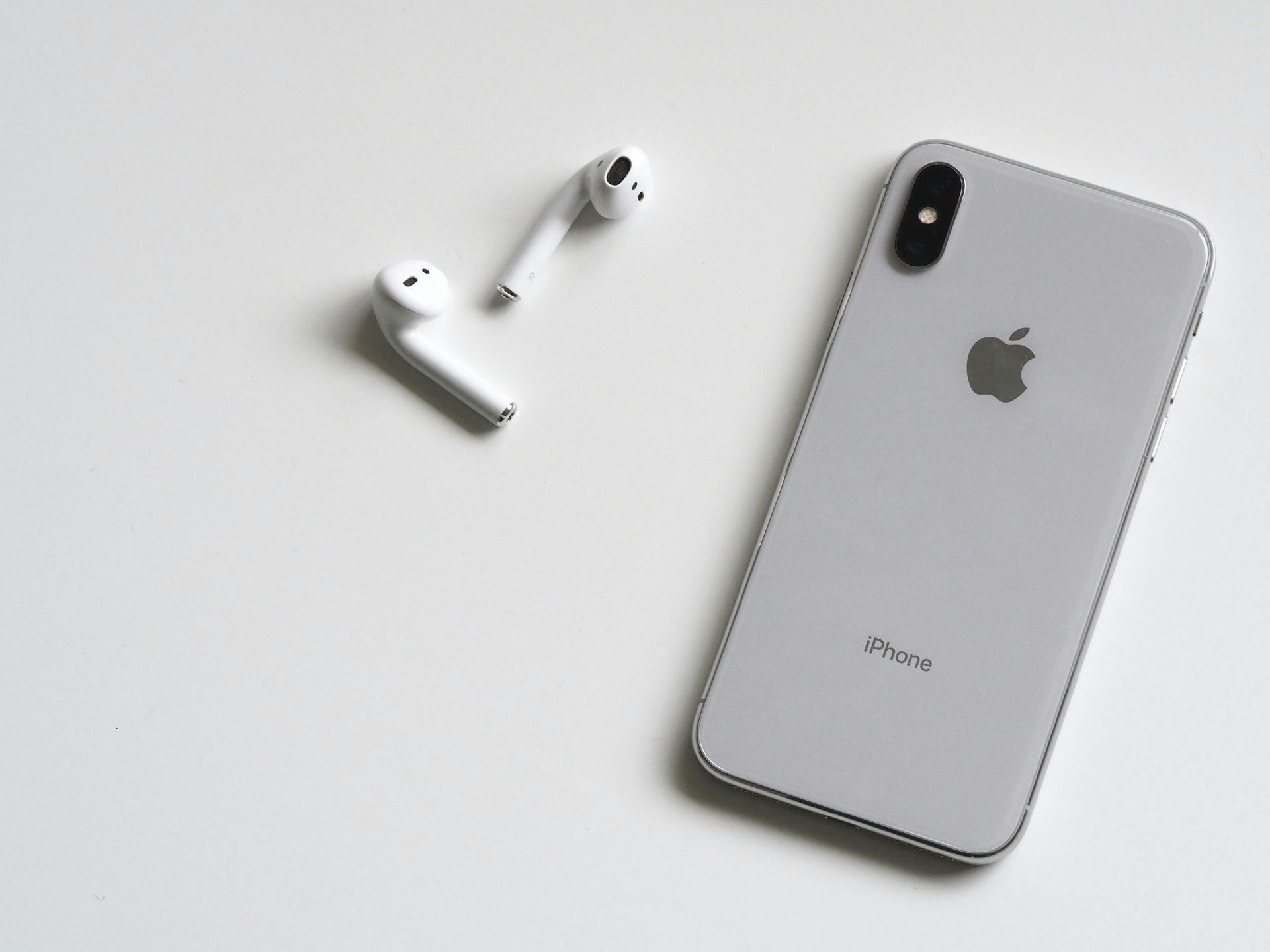 IPhone branco e AirPods em uma superfície branca.