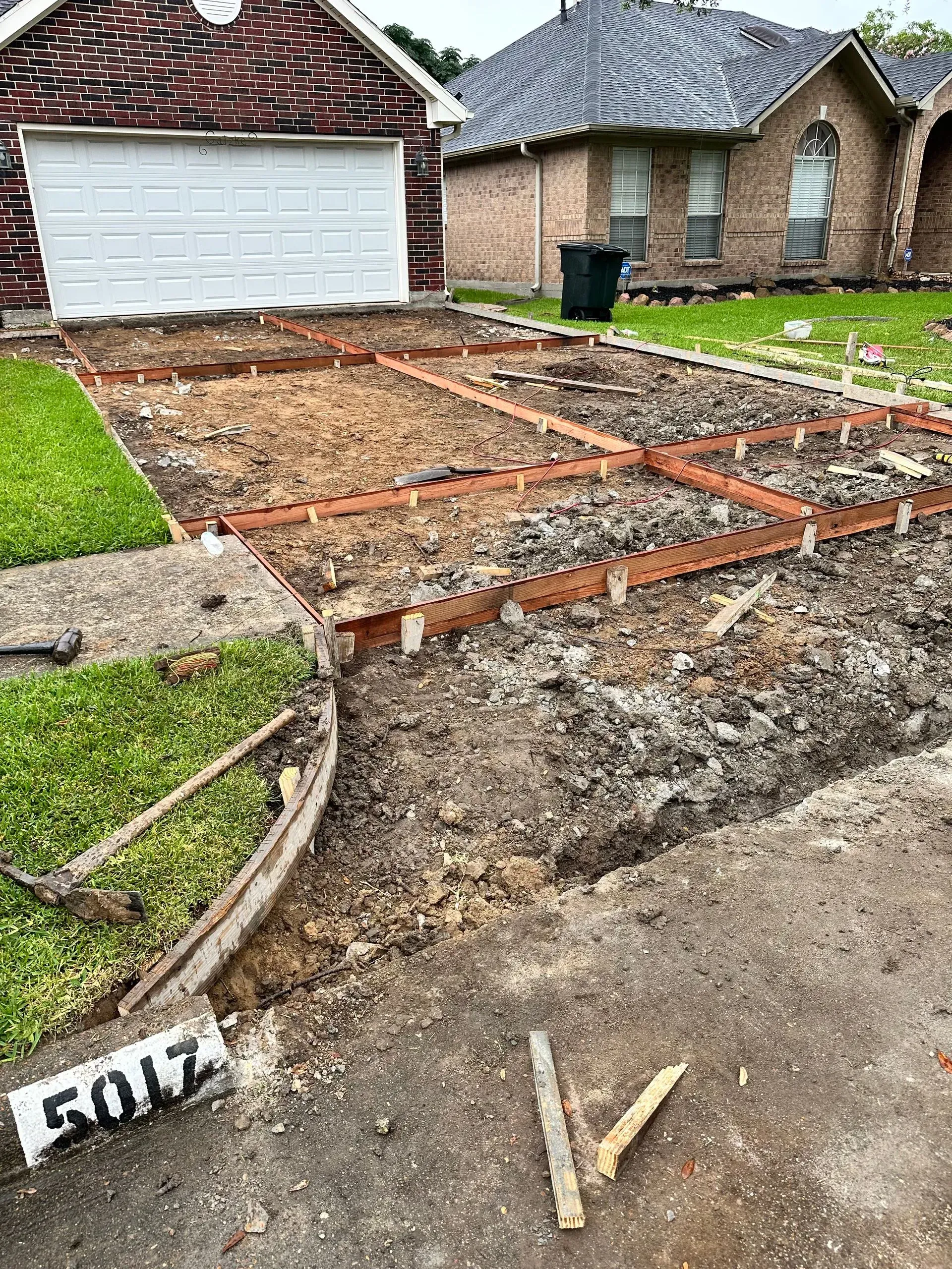 Driveway under construction with wooden forms and exposed soil in front of a house.