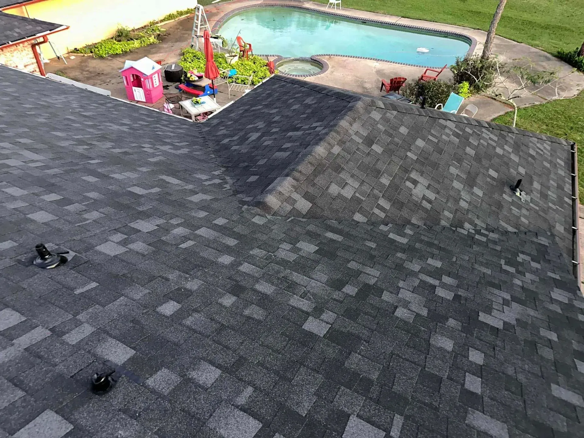 Gray shingle roof of a house with a backyard pool and playground.