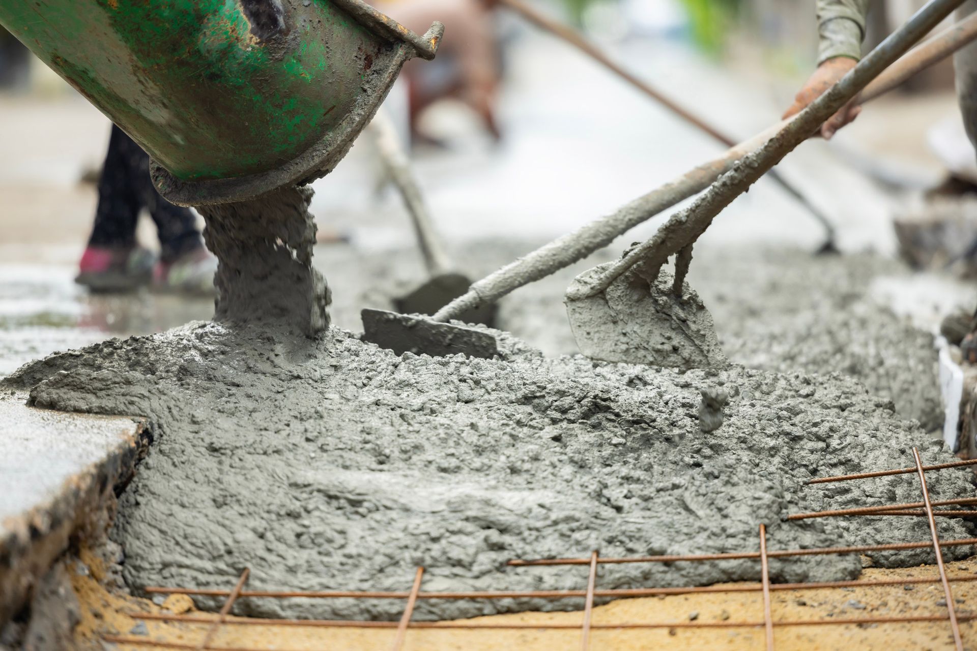 Concrete being poured, leveled with tools, on a sidewalk, over rebar.