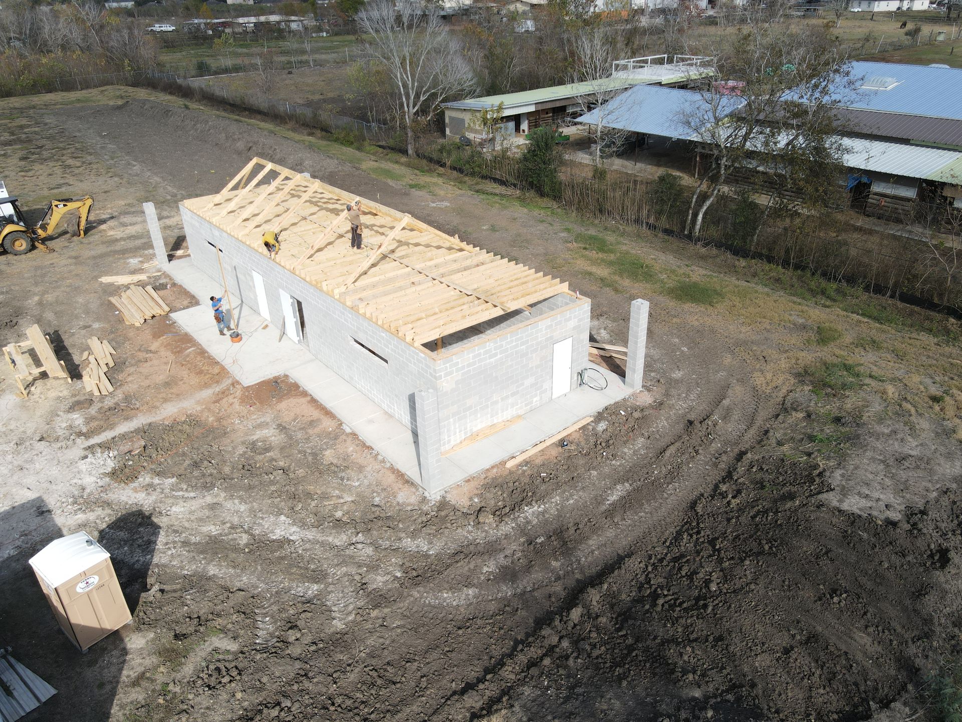 Construction of a rectangular, light-colored block building with wooden roof supports; exterior shot.