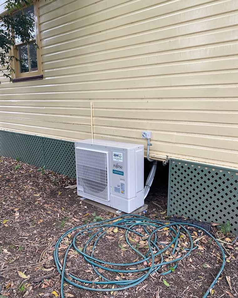 A White Fujitsu Air Conditioner Is Sitting On The Side Of A House — Macleay Air In West Kempsey, NSW