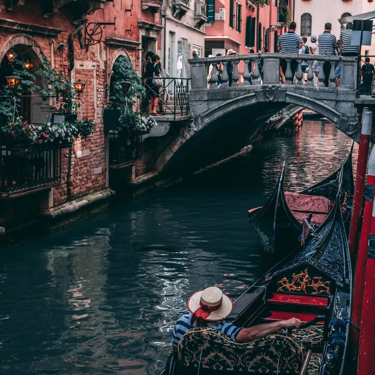 A man in a straw hat is riding a gondola down a canal.