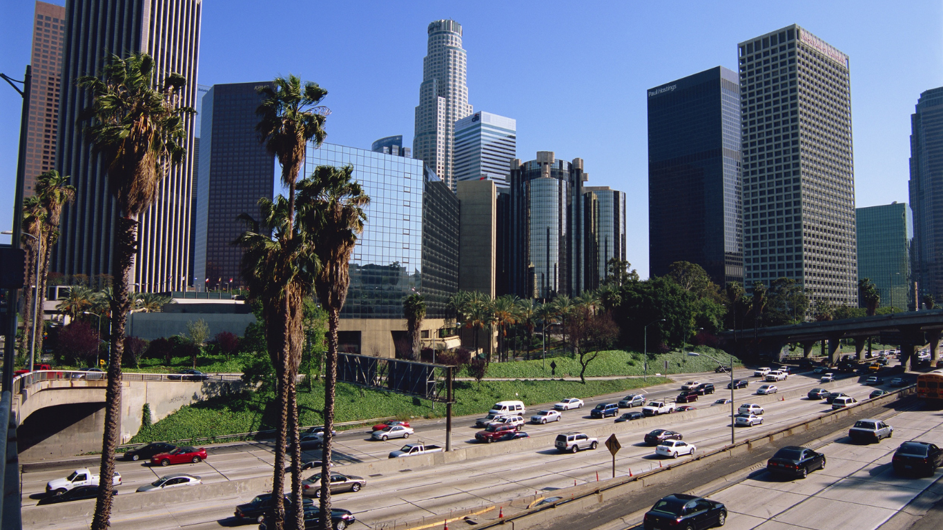 Los Angeles skyline with palm trees, a freeway with cars, and blue sky.