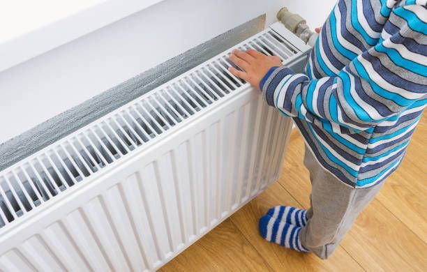 A child is standing next to a radiator in a room.