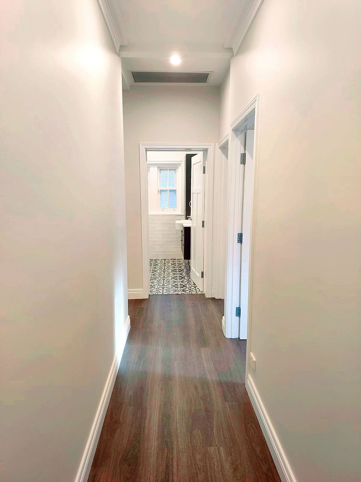 Narrow Hallway With Dark Wood-look Flooring and Doors Leading to Rooms, a Bathroom is Visible Ahead  — Elimar Construction in Goulburn, NSW
