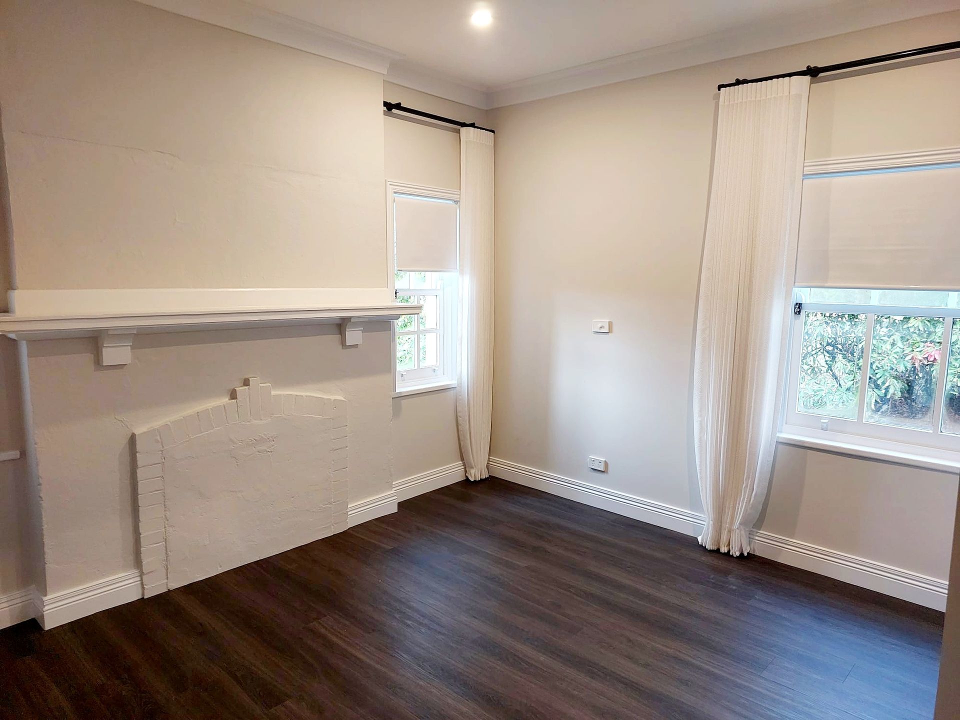 Empty Room With Fireplace, Dark Wood Floor, White Walls, and Two Windows With Sheer Curtains  — Elimar Construction in Goulburn, NSW