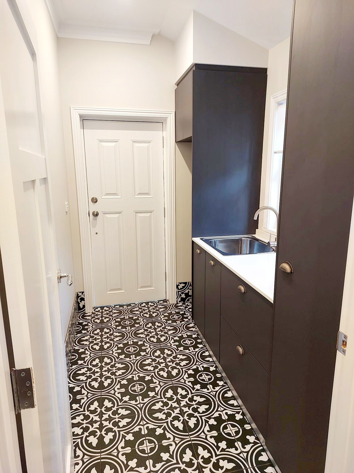 Narrow Laundry Room With Patterned Floor, Dark Cabinets, White Door  — Elimar Construction in Goulburn, NSW