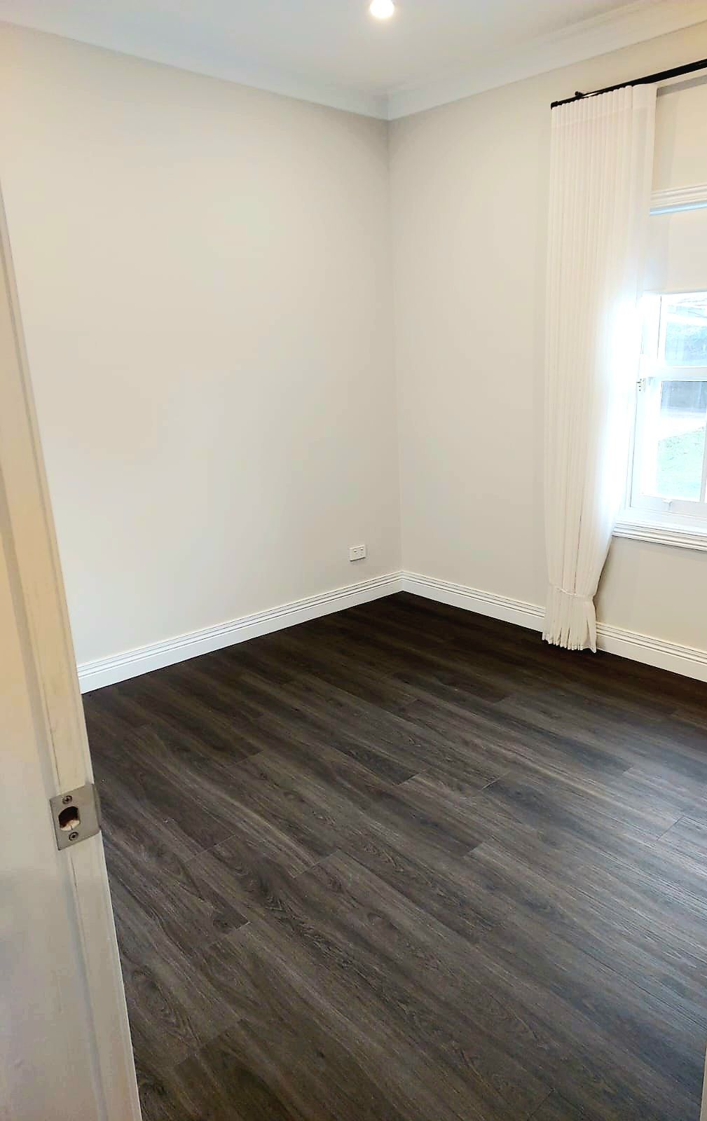 Empty Room With Dark Wood-look Flooring, White Walls, and a Window With Sheer Curtains  — Elimar Construction in Goulburn, NSW